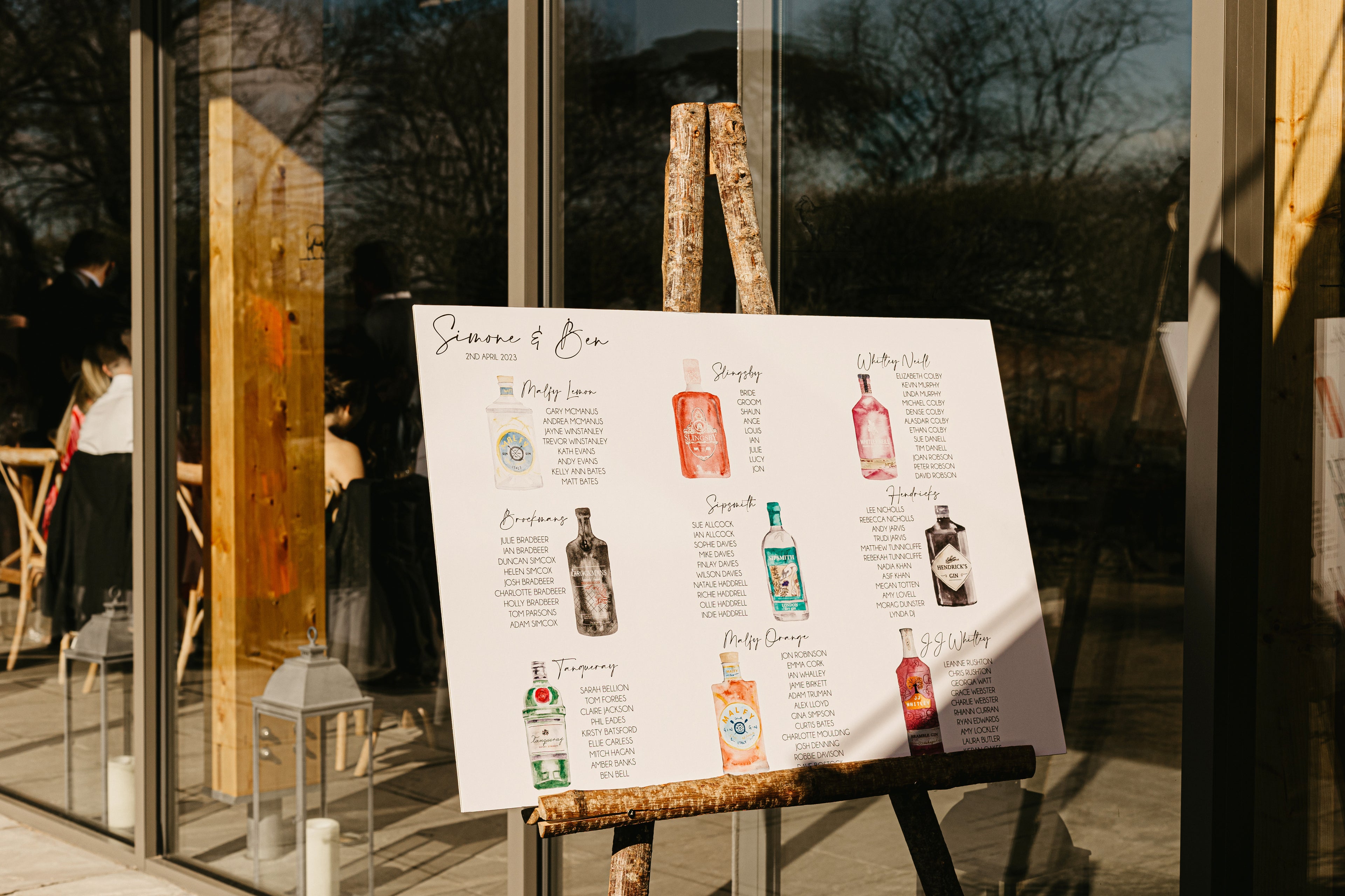 professional photo of a gin bottle themed wedding seating plan on wooden easel outside Thorpe Garden Wedding Venue